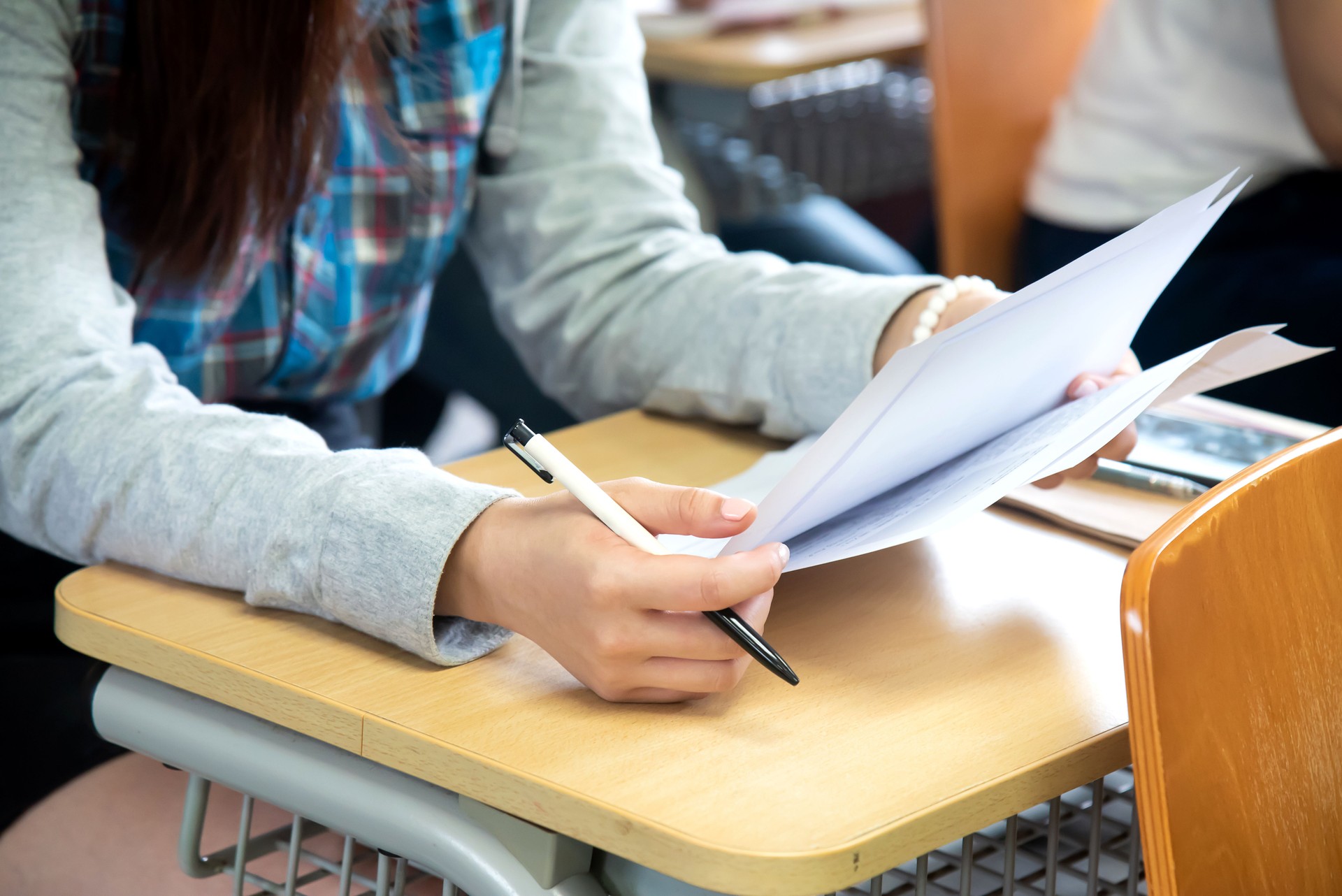 Close-up of female body parts and hands checking her exam papers in classroom