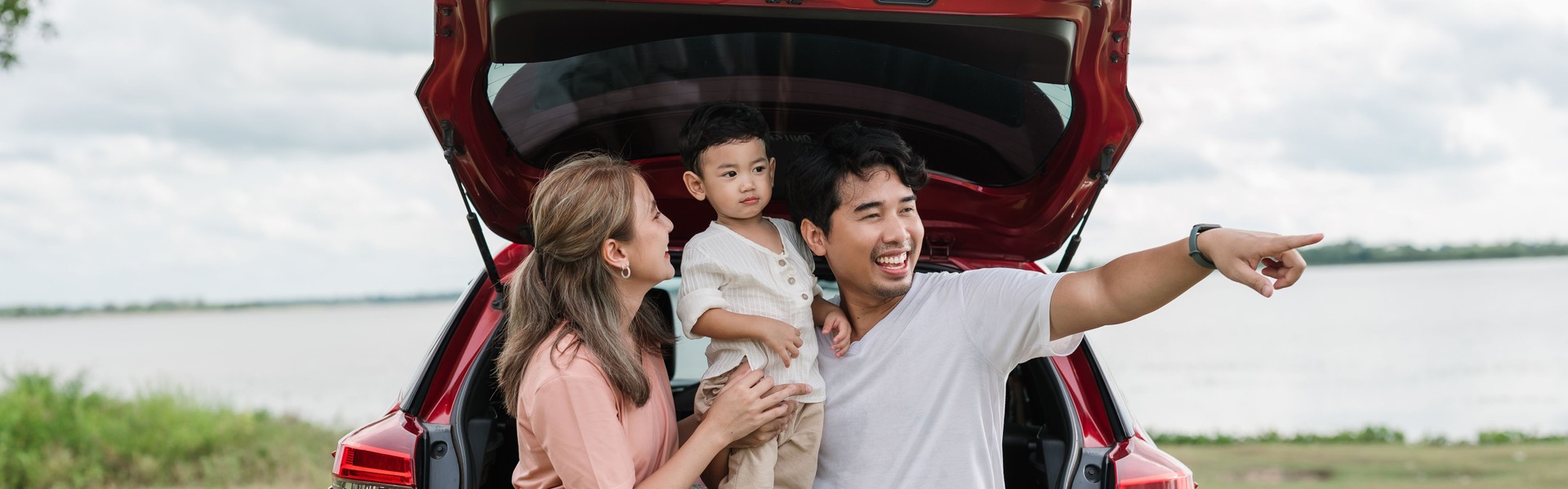 Asian family enjoying a road trip through nature, Father, mother, and little boy relax and sitting on car trunk, taking a break and enjoying view of nature in a peaceful moment.