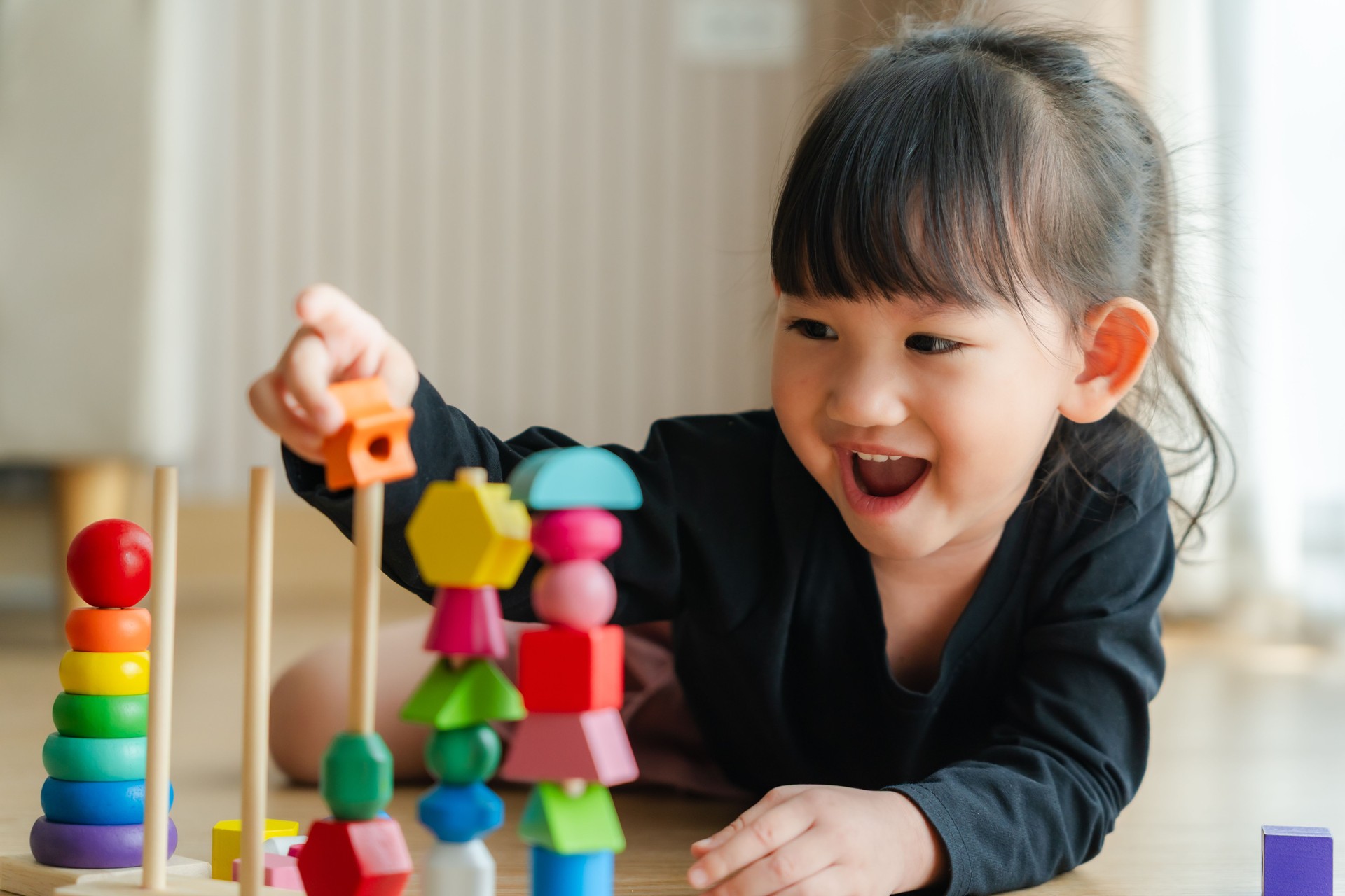 3 year old girl having fun playing with colorful geometric shape wooden blocks educational toys at home. Childhood and kids learning concept.