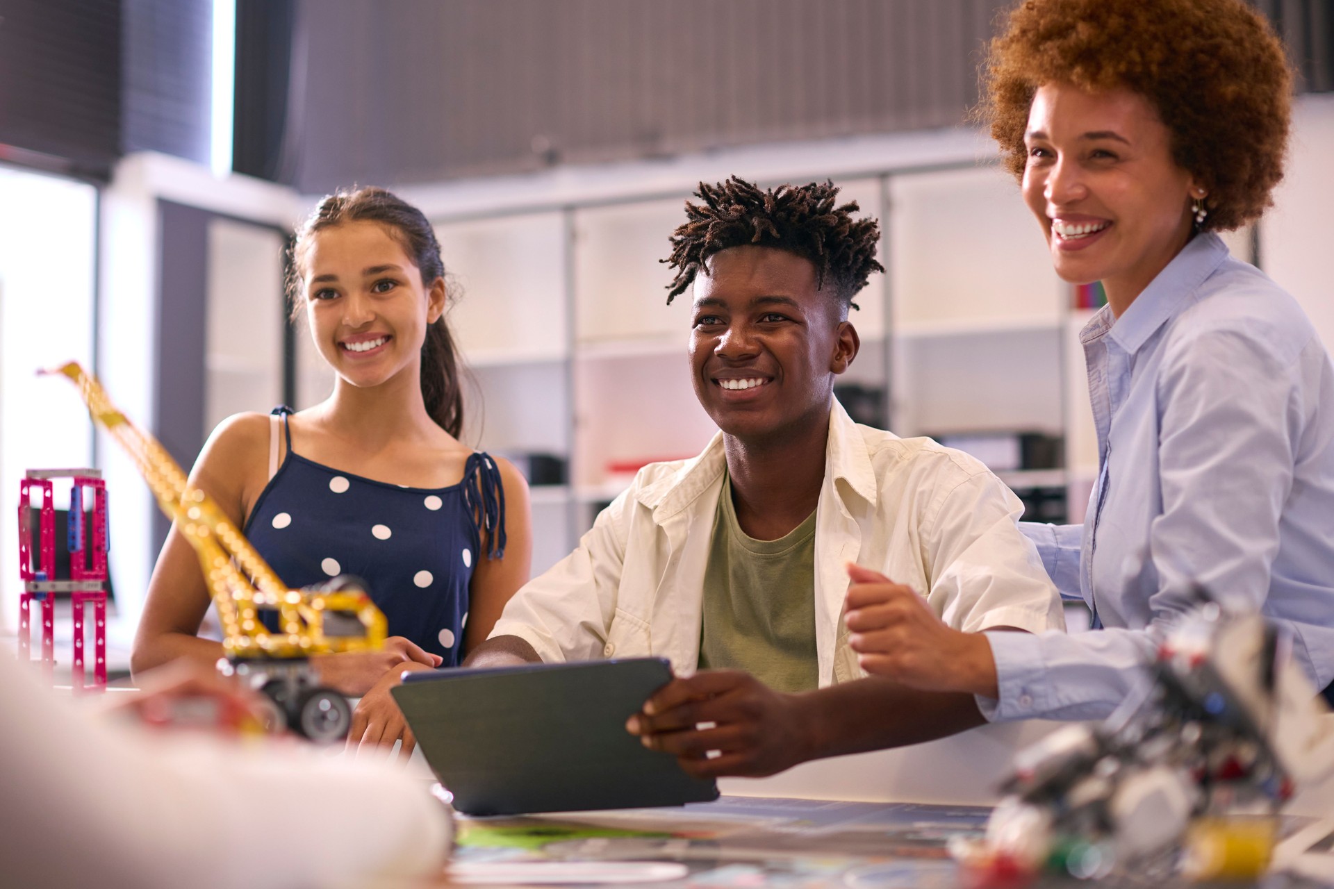 Female High School Teacher With Digital Tablet Helping Students In STEM Technology Lesson